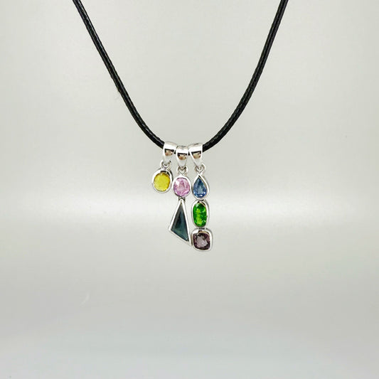 Handcrafted three-pendant gemstone necklace with sapphires, ruby, spinel, and tsavorite (5.81 ct total) on a black leather cord — modular design in white-gold-plated silver.