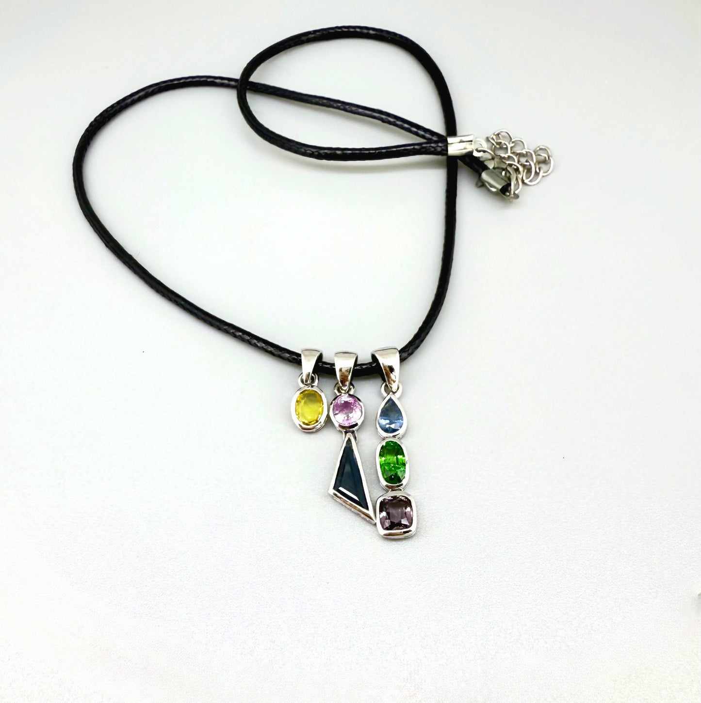 Handcrafted three-pendant gemstone necklace with sapphires, ruby, spinel, and tsavorite (5.81 ct total) on a black leather cord — modular design in white-gold-plated silver.