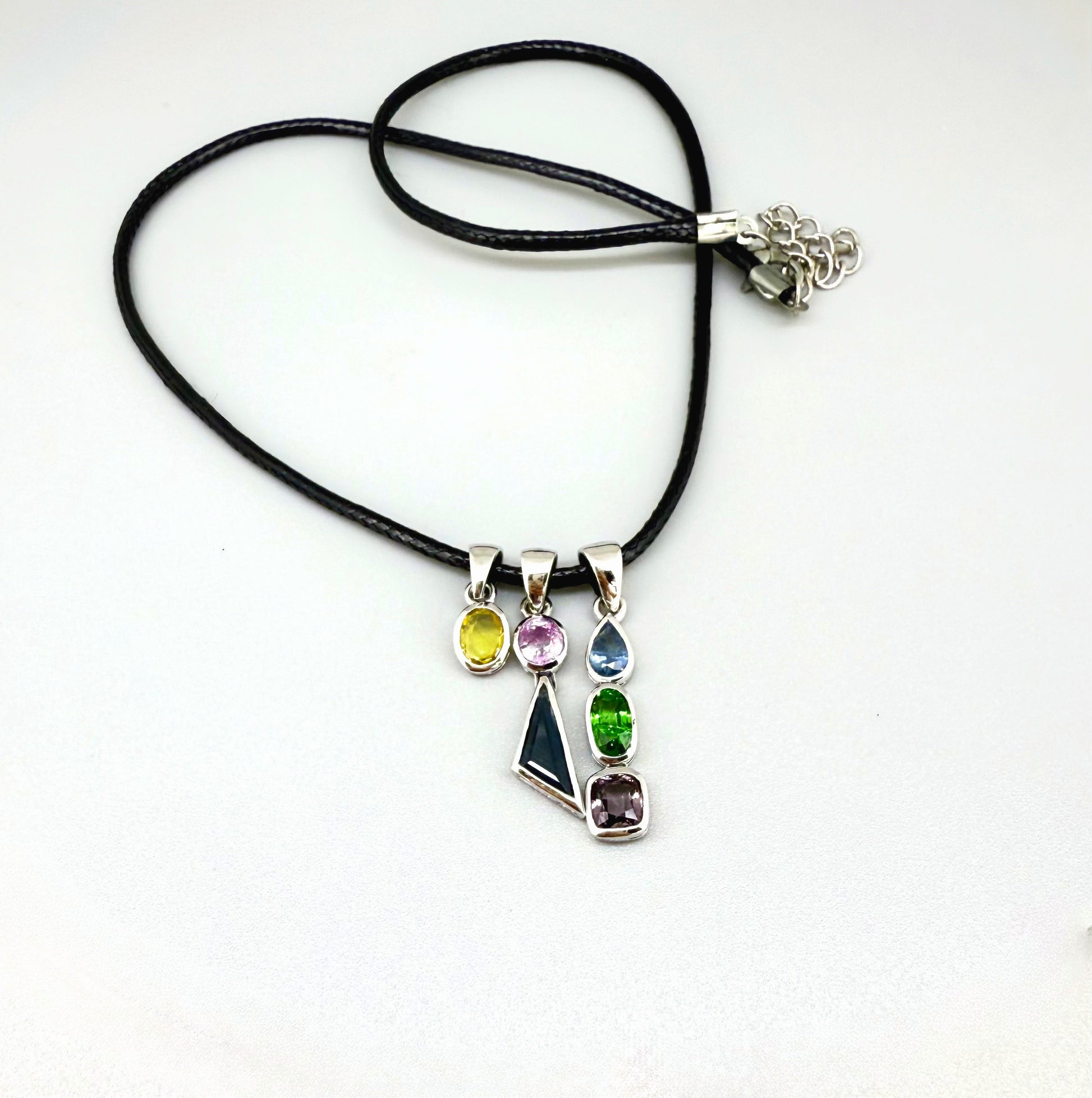 Handcrafted three-pendant gemstone necklace with sapphires, ruby, spinel, and tsavorite (5.81 ct total) on a black leather cord — modular design in white-gold-plated silver.
