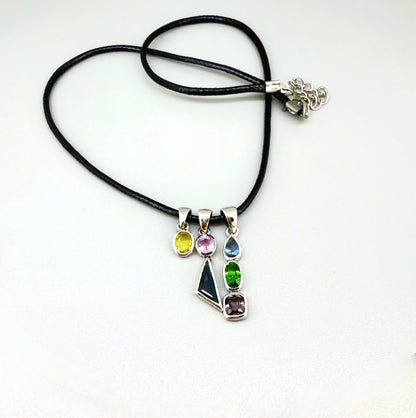 Handcrafted three-pendant gemstone necklace with sapphires, ruby, spinel, and tsavorite (5.81 ct total) on a black leather cord — modular design in white-gold-plated silver.
