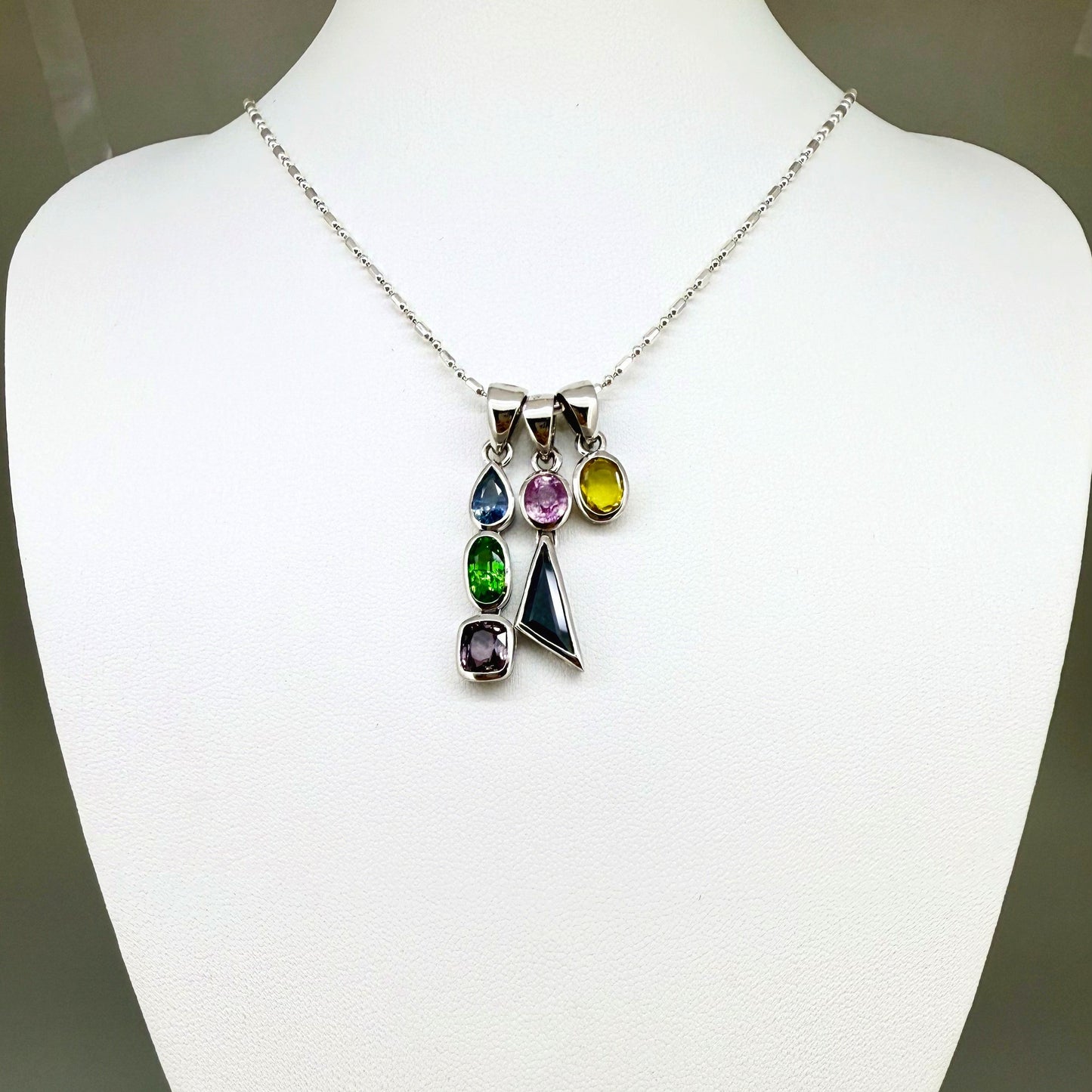 Handcrafted three-pendant gemstone necklace with sapphires, ruby, spinel, and tsavorite (5.81 ct total) on a black leather cord — modular design in white-gold-plated silver.