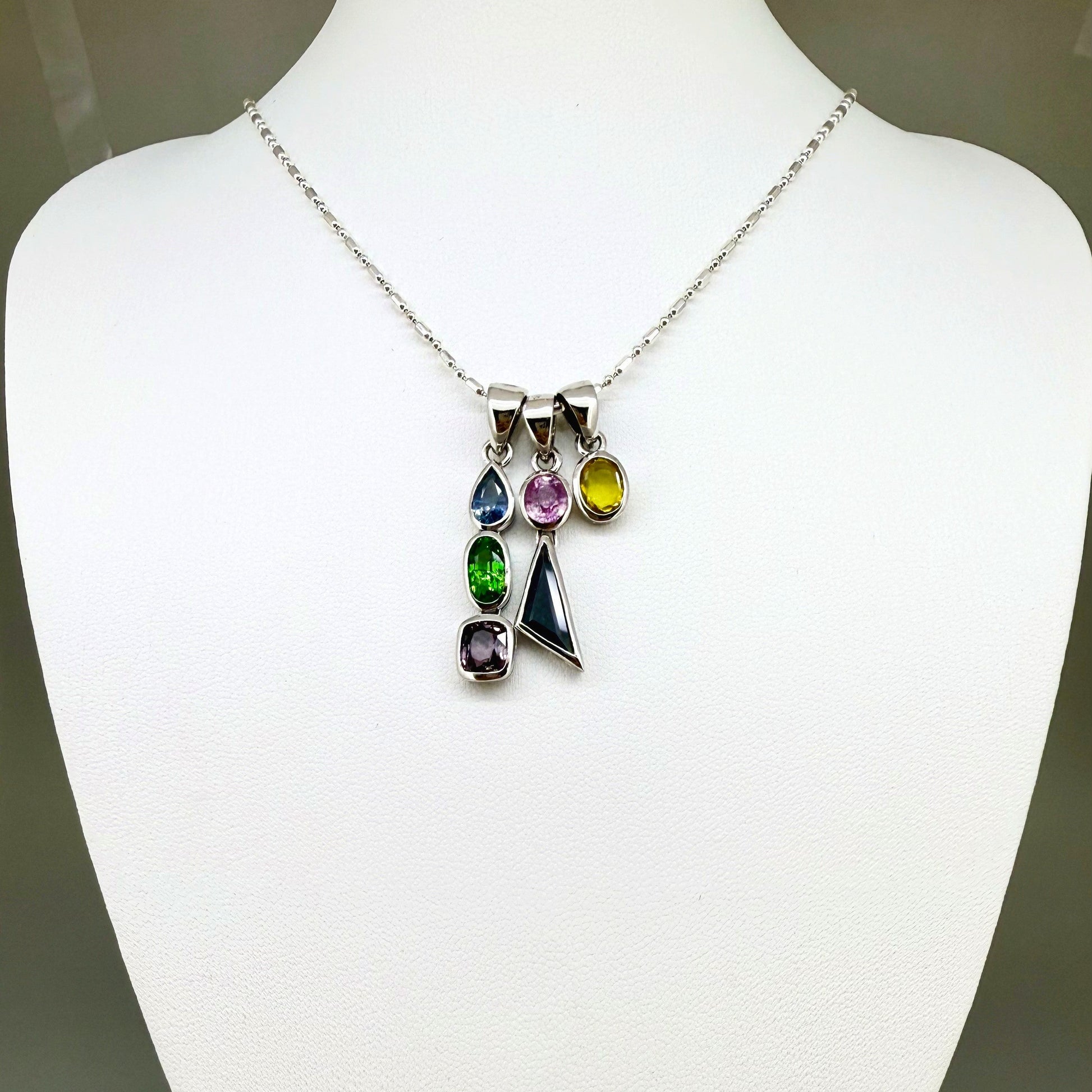 Handcrafted three-pendant gemstone necklace with sapphires, ruby, spinel, and tsavorite (5.81 ct total) on a black leather cord — modular design in white-gold-plated silver.