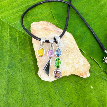 Handcrafted three-pendant gemstone necklace with sapphires, ruby, spinel, and tsavorite (5.81 ct total) on a black leather cord — modular design in white-gold-plated silver.