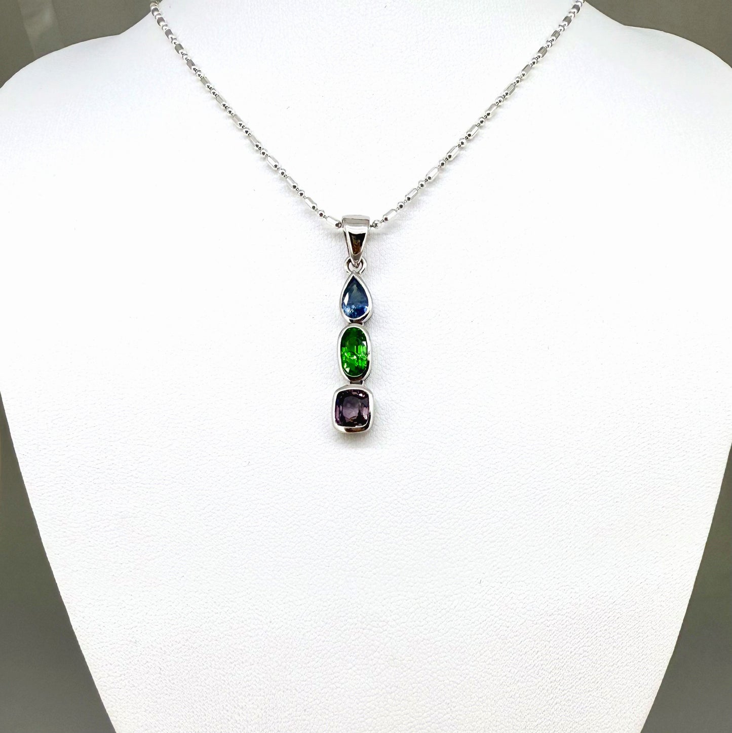 Handcrafted three-pendant gemstone necklace with sapphires, ruby, spinel, and tsavorite (5.81 ct total) on a black leather cord — modular design in white-gold-plated silver.