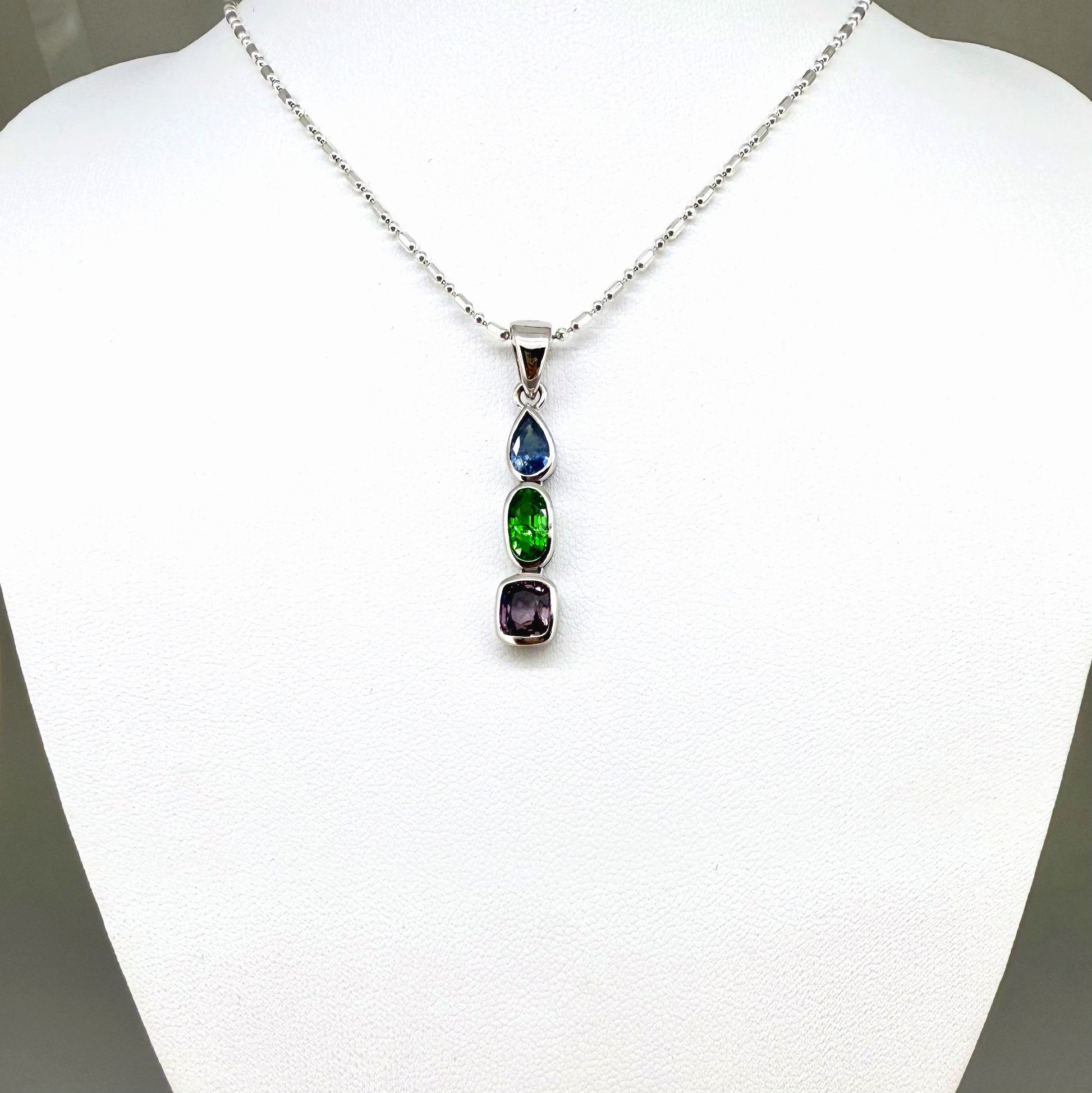 Handcrafted three-pendant gemstone necklace with sapphires, ruby, spinel, and tsavorite (5.81 ct total) on a black leather cord — modular design in white-gold-plated silver.