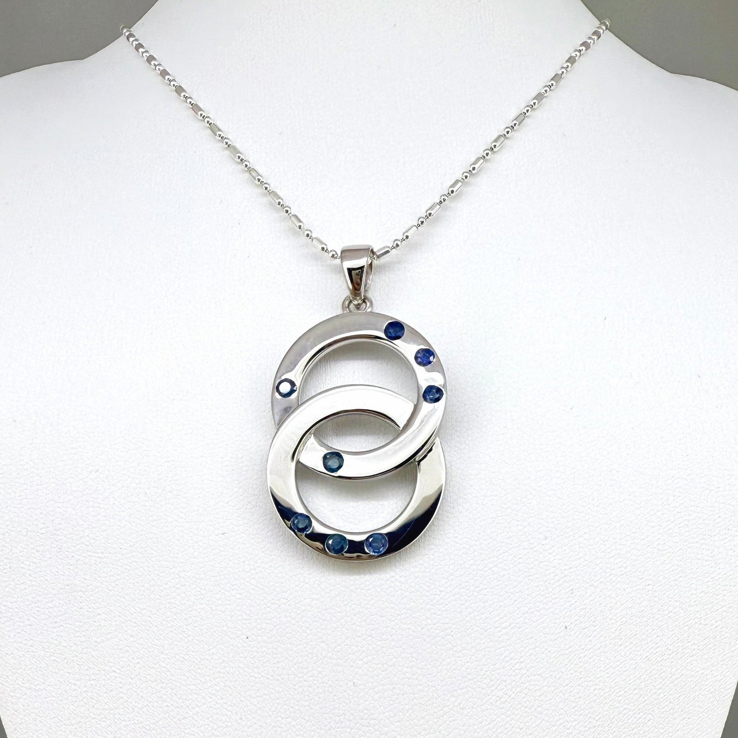 Handcrafted white gold plated silver pendant with 1.14 ct blue sapphires in circular design, symbolizing harmony and elegance.