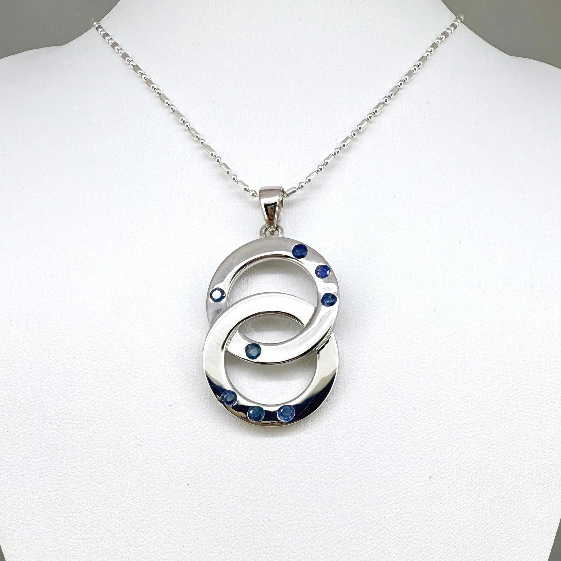 Handcrafted white gold plated silver pendant with 1.14 ct blue sapphires in circular design, symbolizing harmony and elegance.