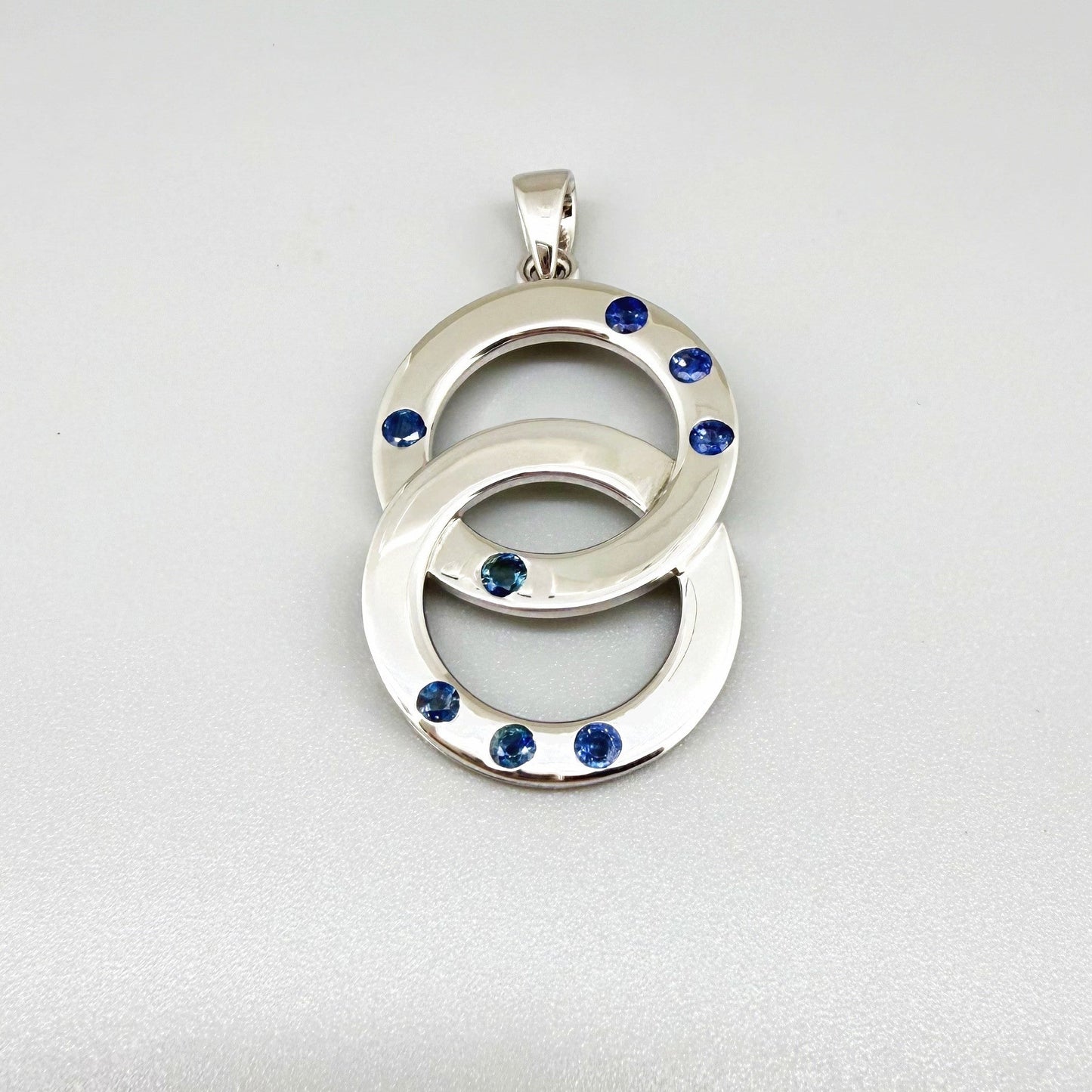 Handcrafted white gold plated silver pendant with 1.14 ct blue sapphires in circular design, symbolizing harmony and elegance.
