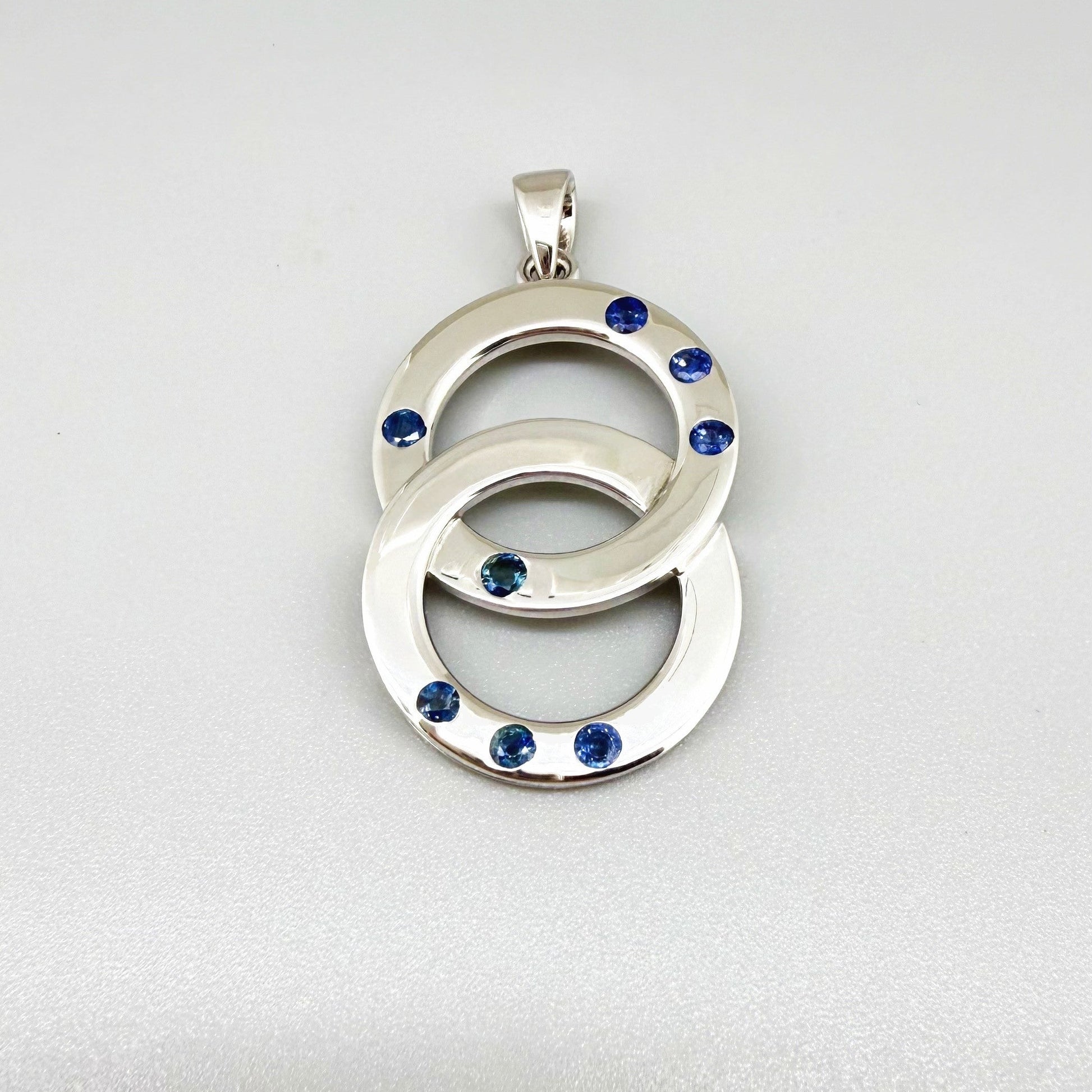 Handcrafted white gold plated silver pendant with 1.14 ct blue sapphires in circular design, symbolizing harmony and elegance.
