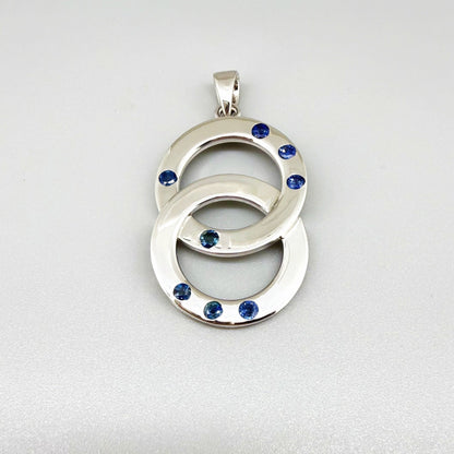 Handcrafted white gold plated silver pendant with 1.14 ct blue sapphires in circular design, symbolizing harmony and elegance.