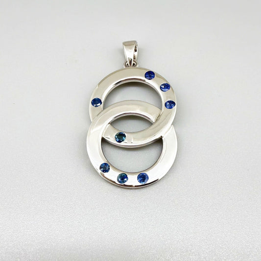 Handcrafted white gold plated silver pendant with 1.14 ct blue sapphires in circular design, symbolizing harmony and elegance.