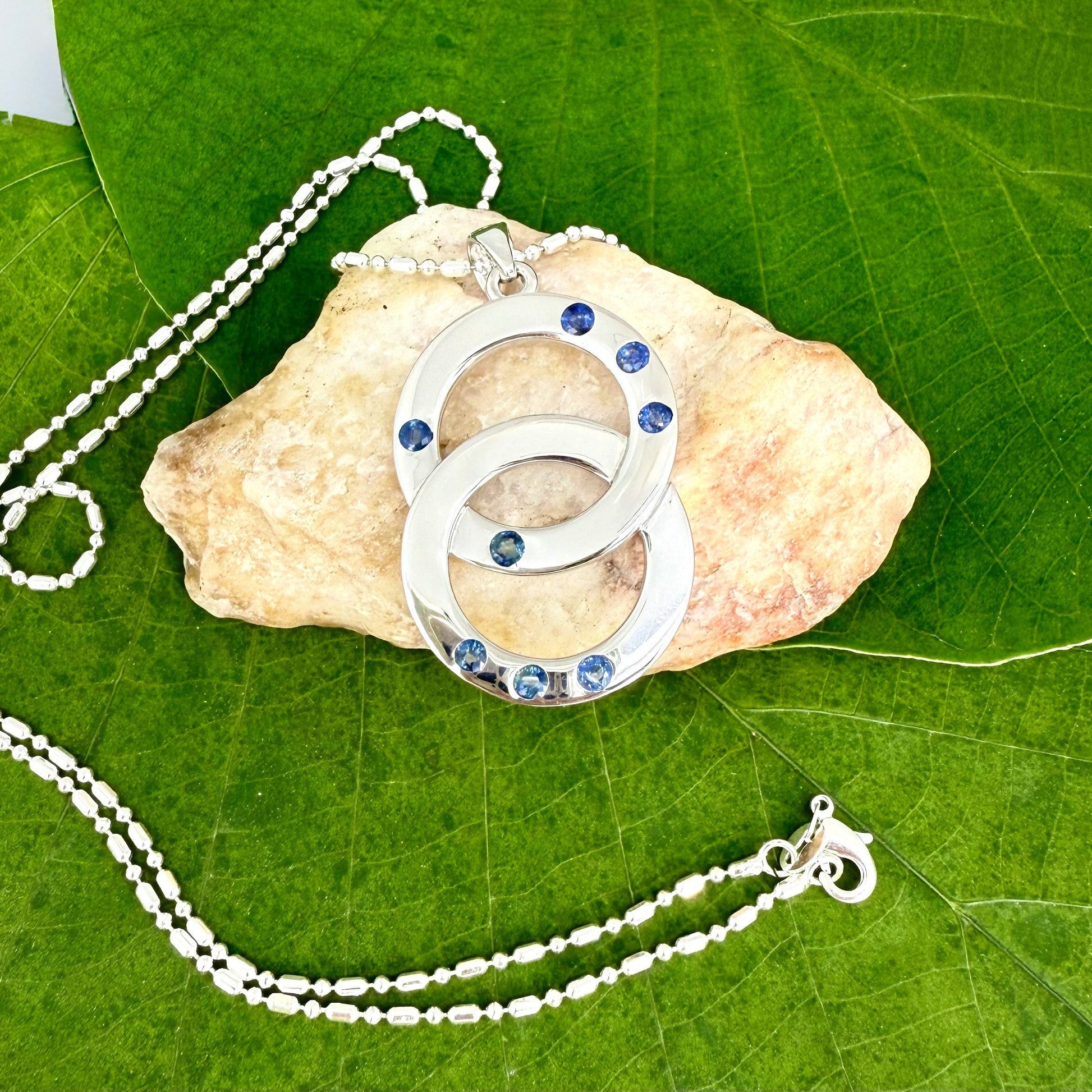 Handcrafted white gold plated silver pendant with 1.14 ct blue sapphires in circular design, symbolizing harmony and elegance.