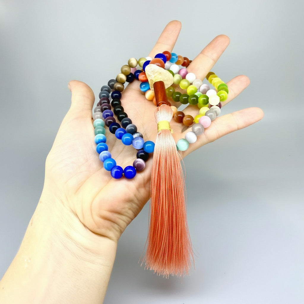 Cat’s Eye mala with 108 polished rainbow-toned beads and a peach-colored tassel, displayed coiled on a light background.