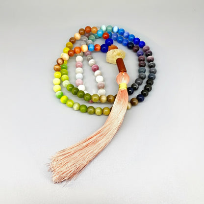 Cat’s Eye mala with 108 polished rainbow-toned beads and a peach-colored tassel, displayed coiled on a light background.