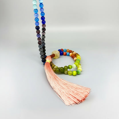 Cat’s Eye mala with 108 polished rainbow-toned beads and a peach-colored tassel, displayed coiled on a light background.