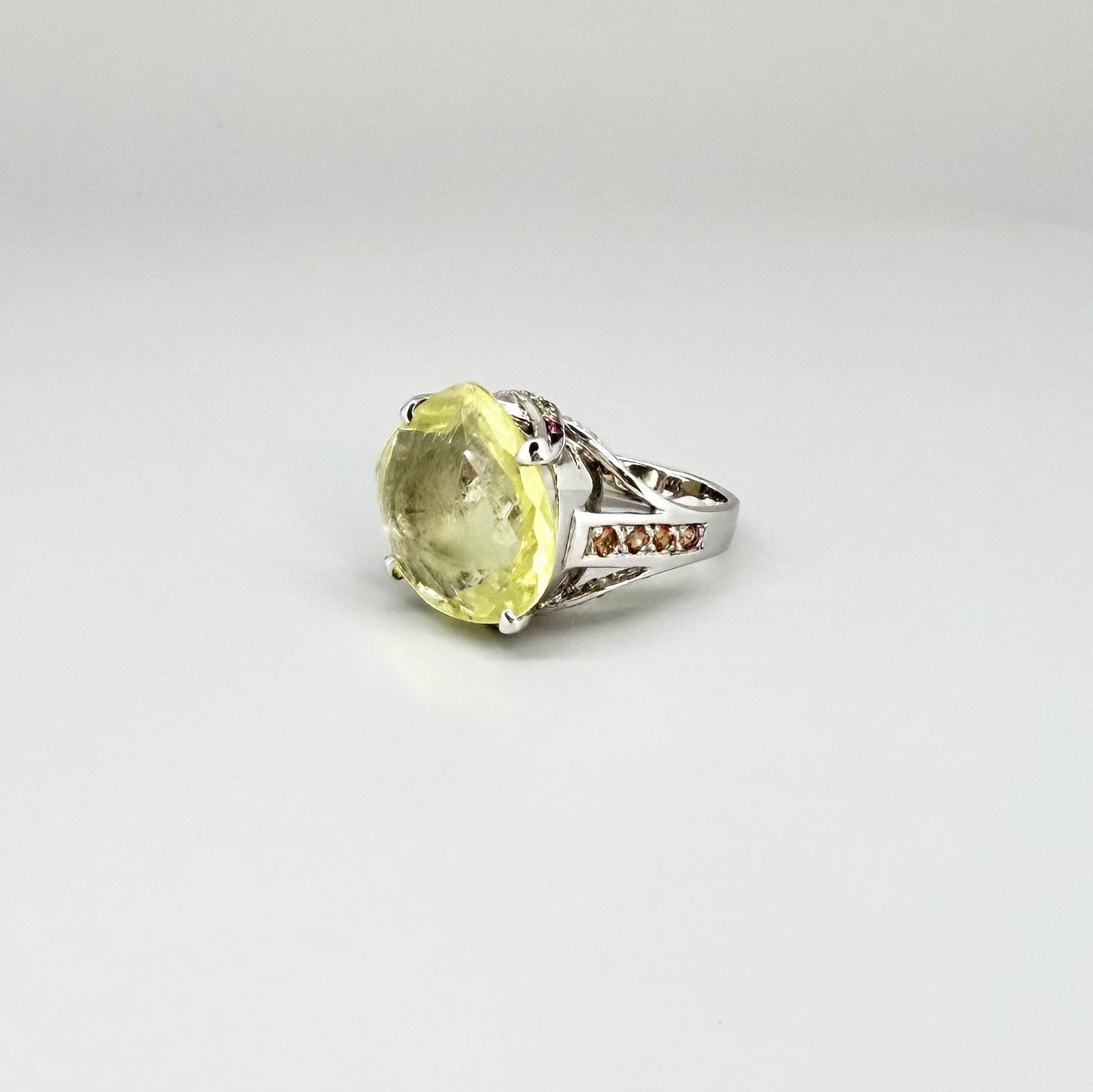 White gold plated sterling silver ring featuring a lemon quartz gemstone surrounded by orange sapphires in a halo design.