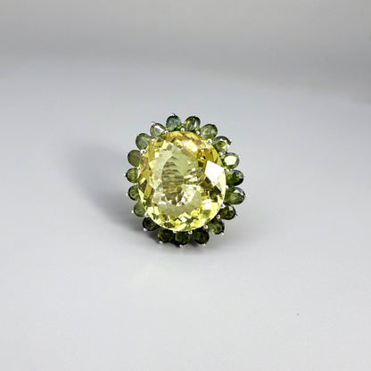 Statement lemon quartz ring in white gold plated sterling silver featuring a large yellow gemstone surrounded by green sapphires in a halo design.