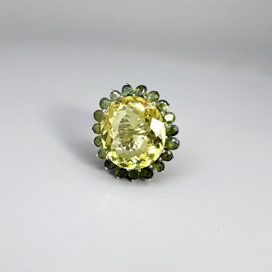 Statement lemon quartz ring in white gold plated sterling silver featuring a large yellow gemstone surrounded by green sapphires in a halo design.