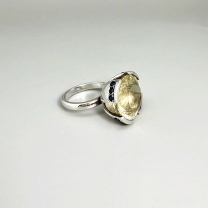 Lemon quartz and sapphire ring in white gold plated sterling silver, featuring a faceted yellow-green gemstone framed by deep blue sapphires, elegant and vibrant design.