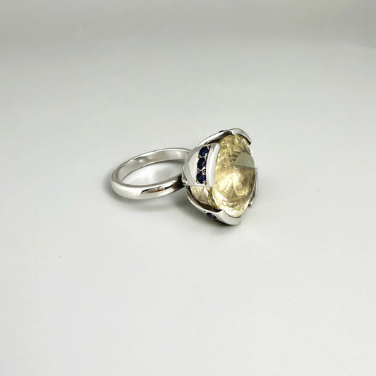 Lemon quartz and sapphire ring in white gold plated sterling silver, featuring a faceted yellow-green gemstone framed by deep blue sapphires, elegant and vibrant design.