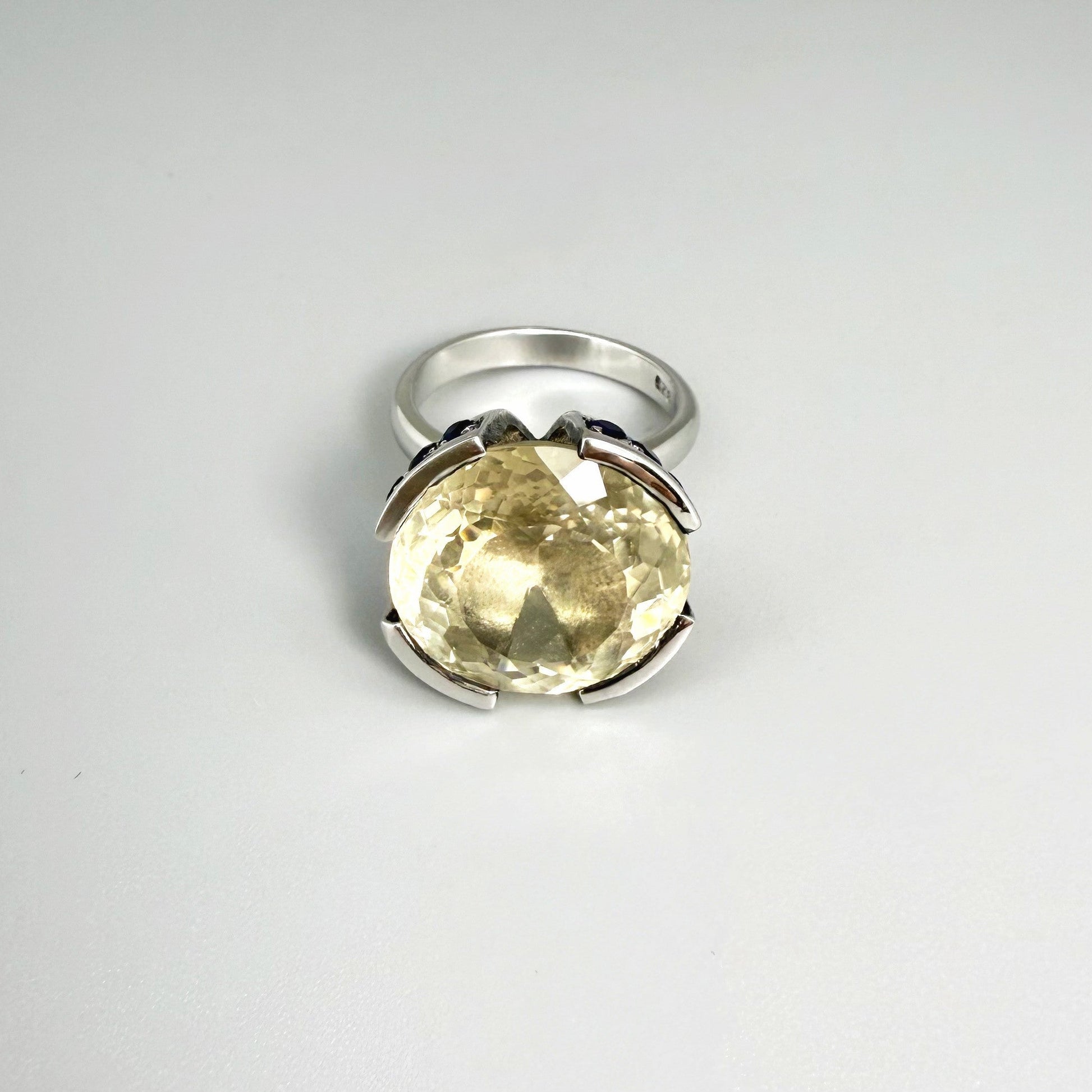 Lemon quartz and sapphire ring in white gold plated sterling silver, featuring a faceted yellow-green gemstone framed by deep blue sapphires, elegant and vibrant design.