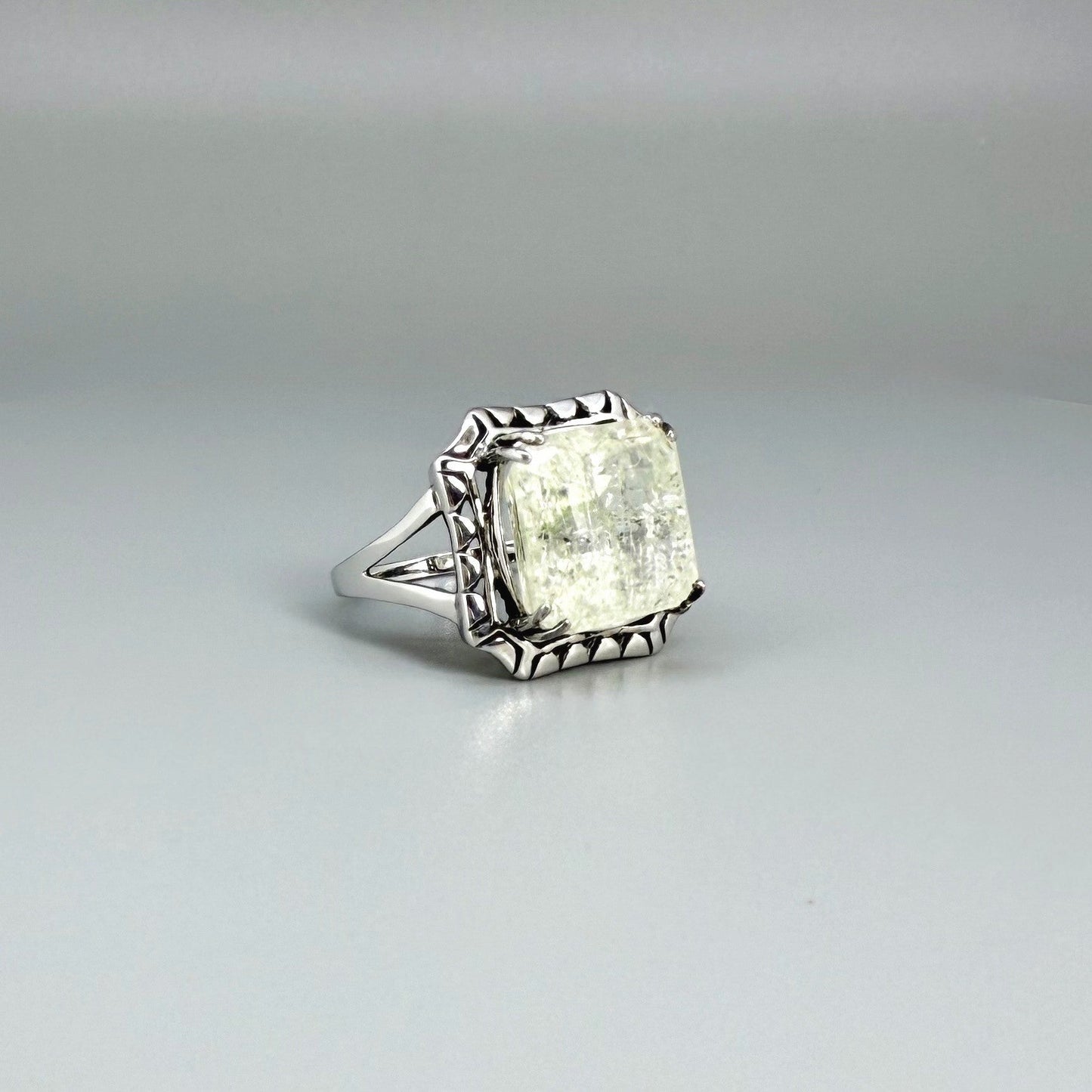 White gold plated sterling silver ring with natural light green emerald, detailed setting, and elegant, refined craftsmanship.