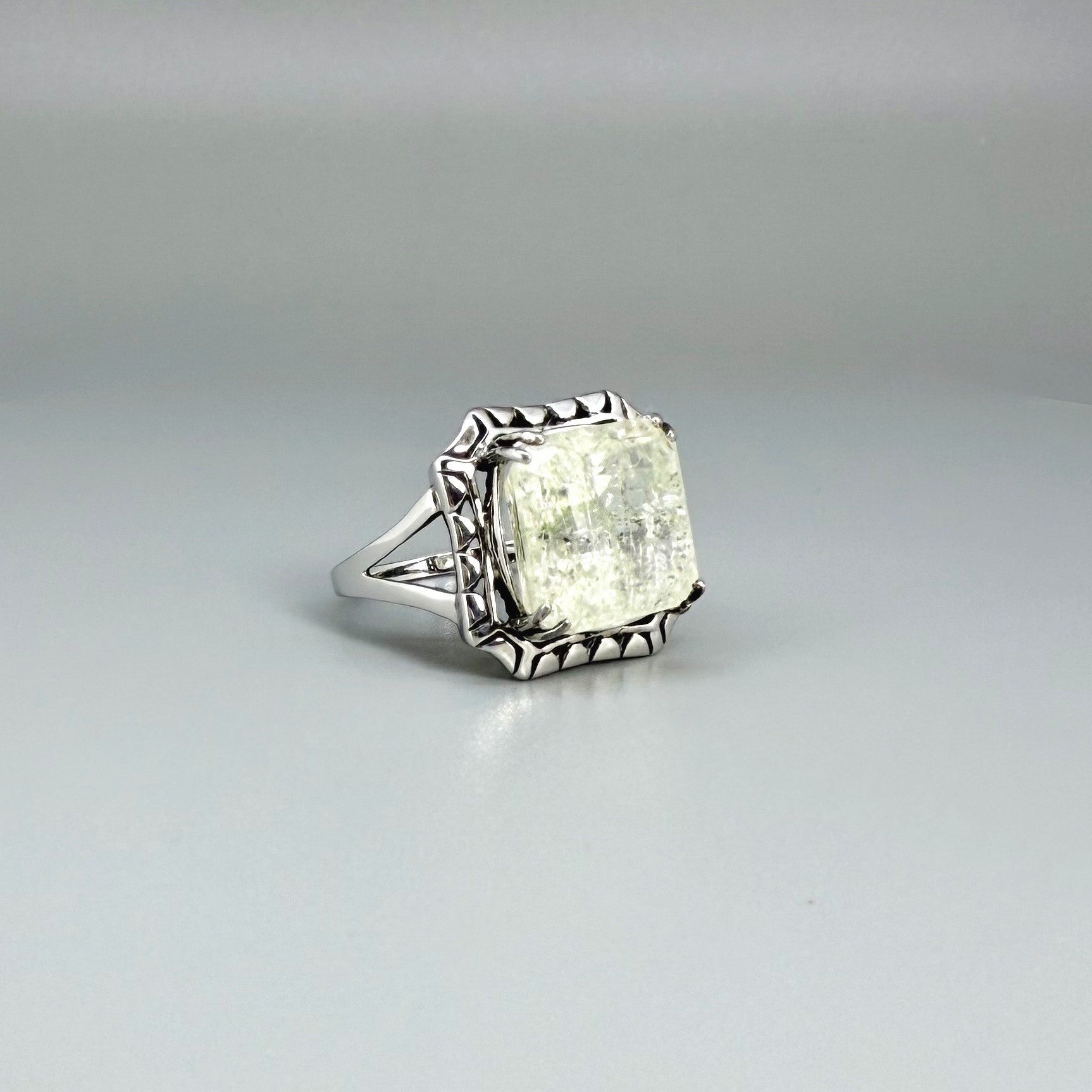 White gold plated sterling silver ring with natural light green emerald, detailed setting, and elegant, refined craftsmanship.
