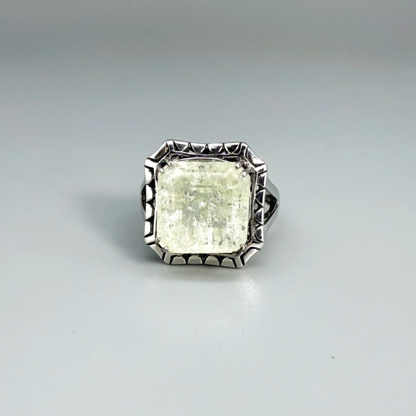 White gold plated sterling silver ring with natural light green emerald, detailed setting, and elegant, refined craftsmanship.