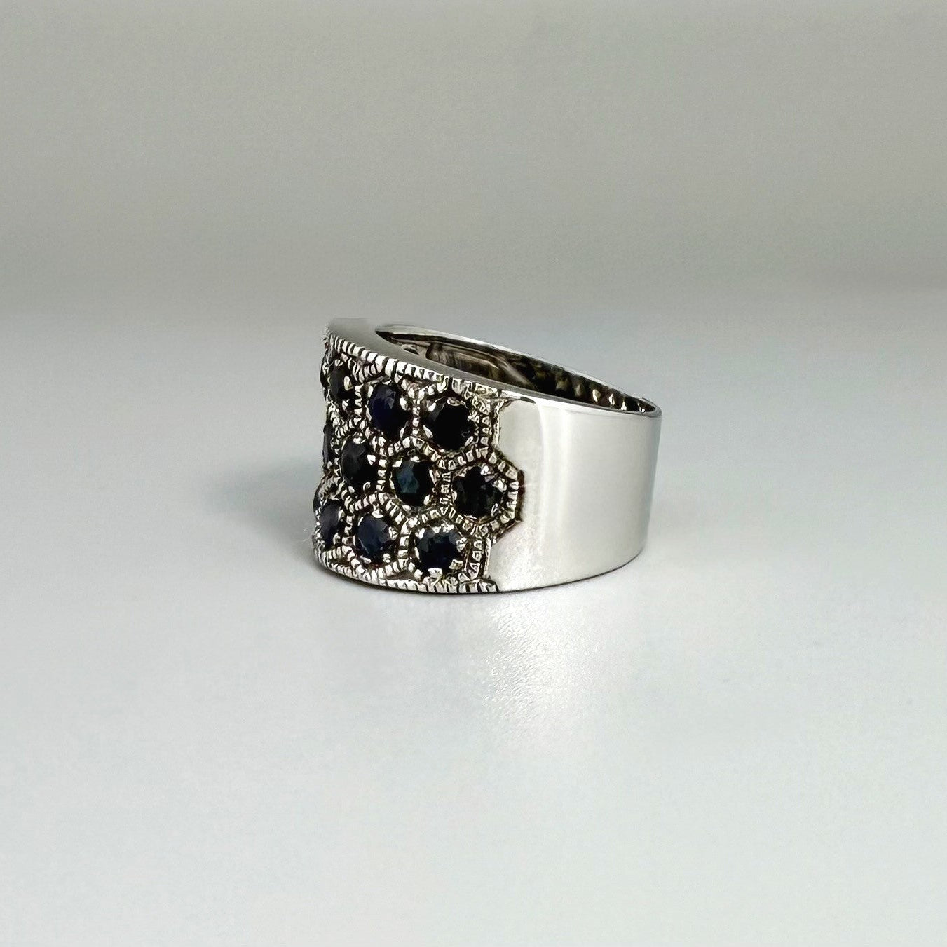 Wide band blue sapphire ring in white gold plated sterling silver featuring faceted deep blue sapphires for an elegant, timeless look.