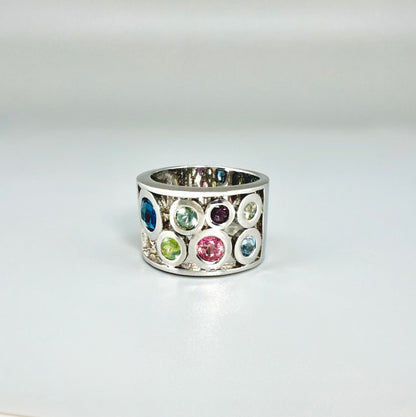 Multicolor sapphire band ring in white gold plated sterling silver, featuring faceted blue, yellow, pink, and green gemstones in elegant wide band design.