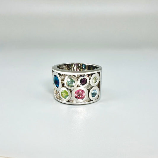 Multicolor sapphire band ring in white gold plated sterling silver, featuring faceted blue, yellow, pink, and green gemstones in elegant wide band design.